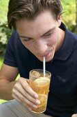 Junger Mann trinkt Eistee mit Strohhalm