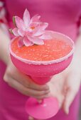 Frau hält pinkfarbenes Glas mit Cocktail, dekoriert mit Blüte