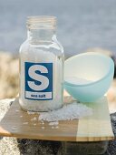 Sea salt in jar on chopping board, sea in background