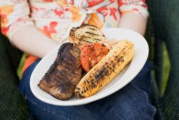 Woman holding plate of grilled steak and accompaniments