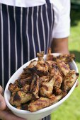 Man in apron holding grilled chicken wings