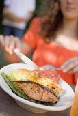Woman eating grilled salmon with corn on the cob & vegetables