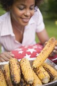 Woman taking grilled corn on the cob out of aluminium dish
