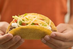 Hands holding a taco filled with mince and cheese