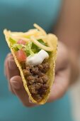 Hand hält Taco mit Hackfleisch, Käse und Klecks Sour Cream