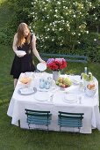 Frau stellt Teller auf gedeckten Tisch im Garten