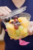 Woman holding plastic tub of fruit salad