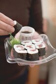 Woman holding maki sushi and soy sauce on plastic tray