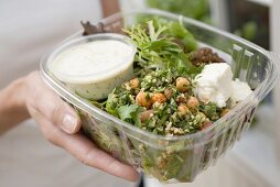 Frau hält Plastikschale mit Salat, Feta und Dressing