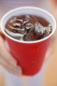 Woman holding beaker of cola with ice cubes