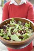 Woman holding large bowl of salad leaves with nuts