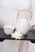 Woman holding teapot, tea bowl and water lily on tray
