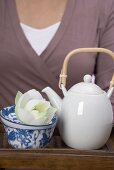 Frau hält Tablett mit Teekanne, Teeschale und Blüte