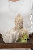 Woman holding statue of Buddha, candle and orchid on tray
