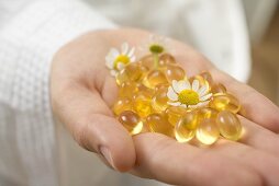 Hand holding vitamin capsules and chamomile flowers