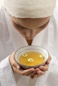 Woman holding bowl of chamomile tea with flowers