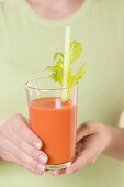 Woman holding glass of carrot juice with celery and straw