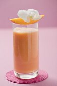 Glass of mango smoothie with wedge of mango and orchid