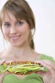 Frau hält gesundes Sandwich mit Avocado und Sprossen