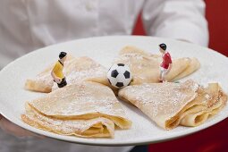 Woman serving plate of sweet crêpes with football figures