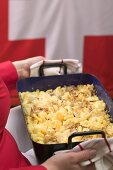 Frau serviert Nudelauflauf mit Käse und Zwiebeln (Schweiz)