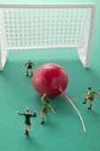 Toy footballers with radish in front of goal