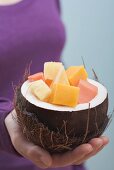 Woman holding hollowed-out coconut full of exotic fruit salad