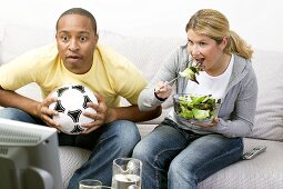 Paar mit Fussball und Salat vor dem Fernseher