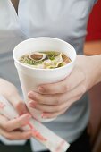 Woman holding paper cup of Asian noodle soup