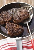 Three peppered steaks in frying pan