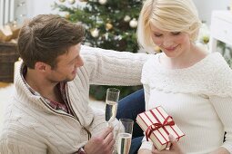 Mann und Frau halten Sektgläser und Weihnachtsgeschenk