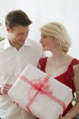 Woman holding large Christmas parcel, man holding glass of wine