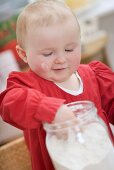 Toddler reaching into jar of flour