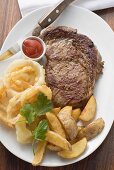 Rib-eye steak with onion rings, ketchup and potato wedges