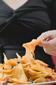 Hand taking tortilla chip with melted cheese from plate