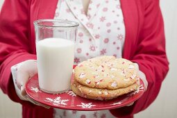 Woman holding Christmas cookies and glass of milk on plate