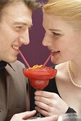 Romantic couple drinking Strawberry Daiquiri out of one glass