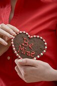 Woman holding chocolate heart with the words Be Mine