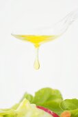 Olive oil dripping from a spoon onto salad