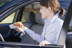 Junge Frau mit Croissant in der Hand steigt ins Auto