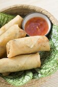 Spring rolls and chilli sauce on leaves in basket