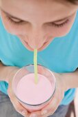 Junge Frau trinkt Erdbeermilch mit Strohhalm (Close Up)