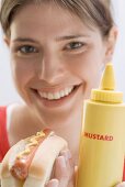 Junge Frau hält Hot Dog und Senfflasche
