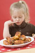 Kleines Mädchen betrachtet Teller mit Hähnchenkeulen