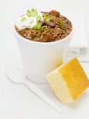 Chili con carne with sour cream in polystyrene cup, cornbread