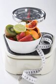 Bowl of fresh fruit and tape measure on scales