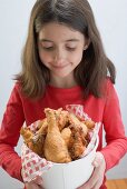 Little girl holding deep-fried chicken drumsticks