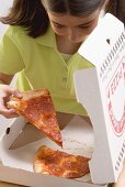 Kleines Mädchen nimmt Pizzastück aus Pizzakarton