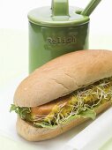 A hot dog with sprouts beside a relish pot
