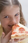 Girl biting into a slice of salami pizza